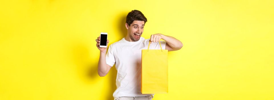 Happy man looking at shopping bag and showing mobile phone screen. Concept of online banking and money.