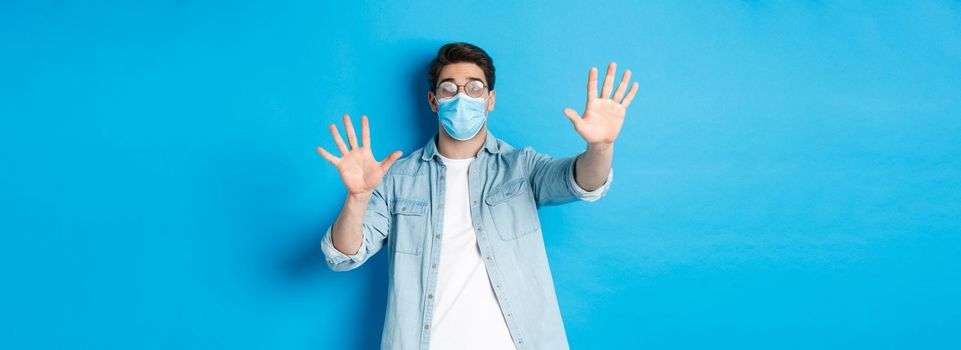 Concept of coronavirus, social distancing and pandemic. Man in medical glass cant see in foggy glasses, standing over blue background.