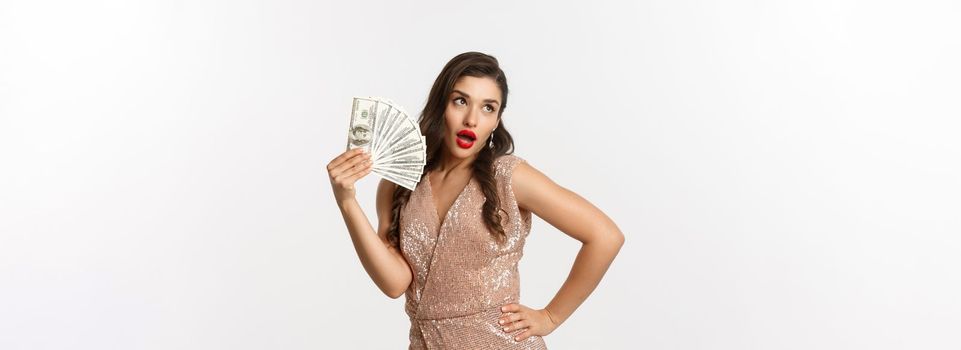 Shopping concept. Successful attractive woman in elegant dress showing dollars, bragging with money, standing over white background.