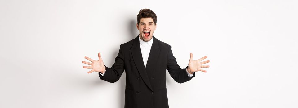 Portrait of pissed-off and frustrated businessman in suit, shouting angry and shaking hands, standing distressed against white background.