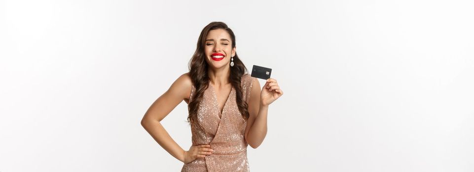 Holidays. christmas party and shopping concept. Satisfied woman in elegant dress rejoicing while showing credit card, smiling happy, standing over white background.