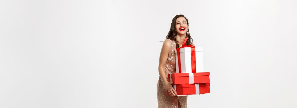 Party and celebration concept. Full-length of attractive brunette in glamour dress, holding Christmas gifts and laughing happy, white background.