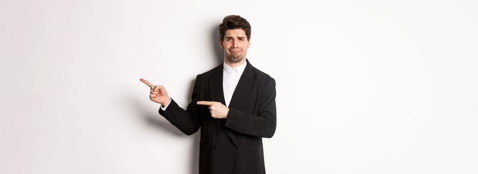 Image of devestated man in party suit, crying and complaining, pointing fingers right at something disappointing, standing over white background.