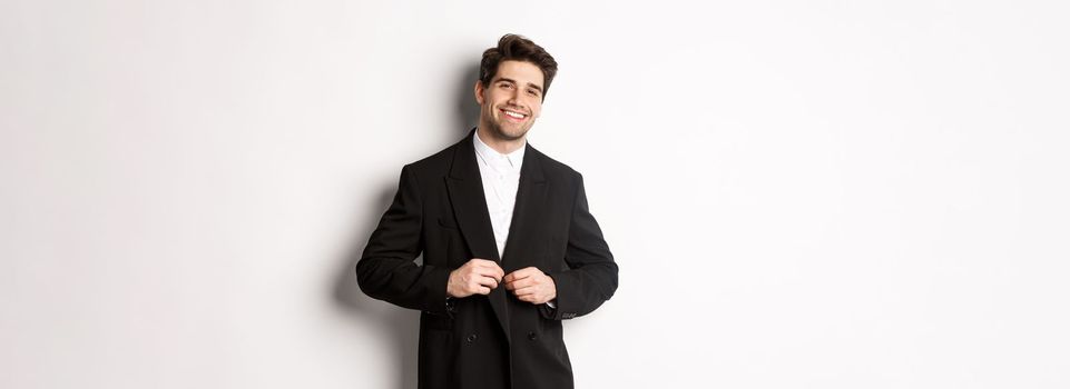 Image of handsome and confident businessman with beard, button down jacket and smiling, standing against white background.