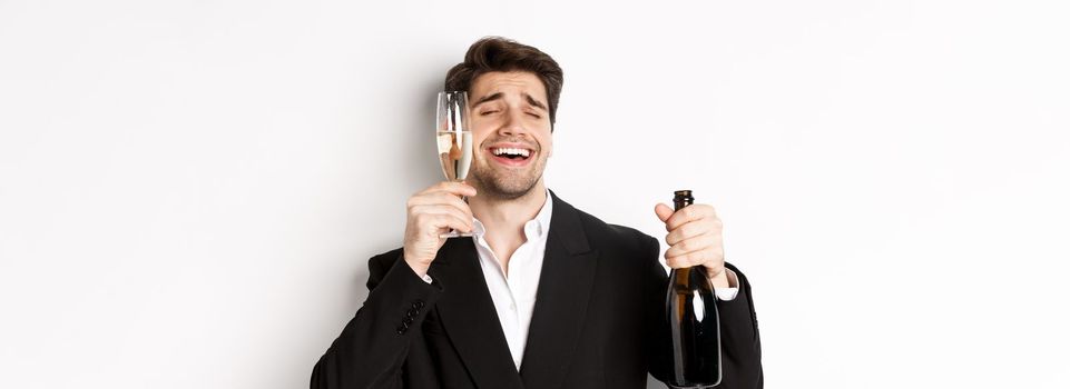 Close-up of handsome drunk guy in suit, holding glass of champagne and celebrating new year, standing over white background.