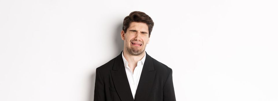 Close-up of miserable man in suit, crying and sobbing, feeling sad, standing against white background.