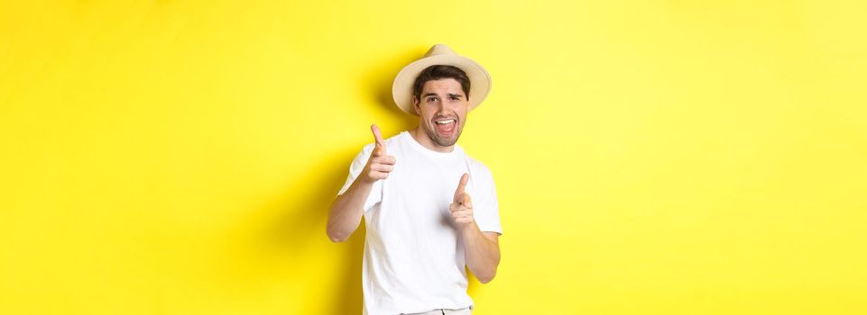 Concept of tourism and vacation. Happy cool guy pointing fingers at you, standing over yellow background.