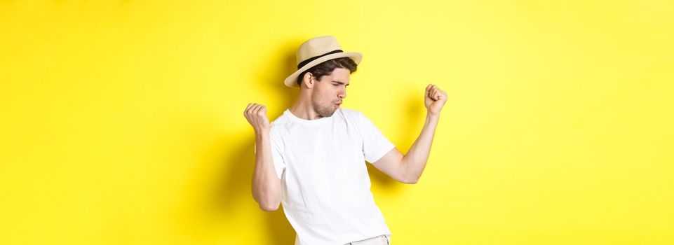 Concept of tourism and vacation. Lucky guy tourist rejoicing, making fist pump and saying yes, standing pleased against yellow background.