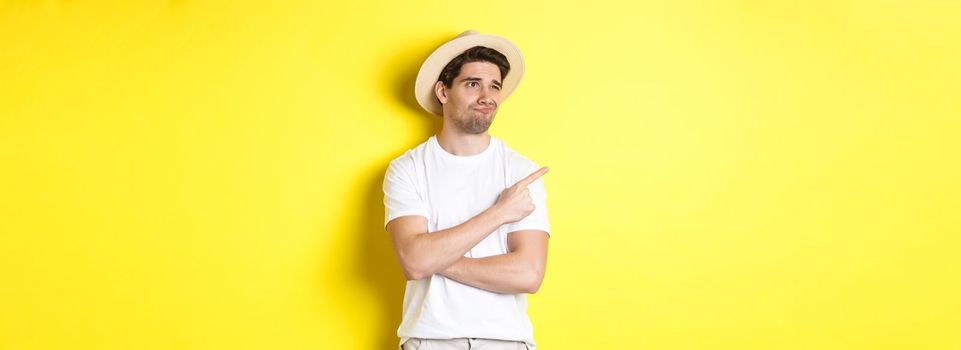 Concept of tourism and lifestyle. Displeased male tourist complaining, looking and pointing finger at upper left corner promo with disappointment, standing against yellow background.