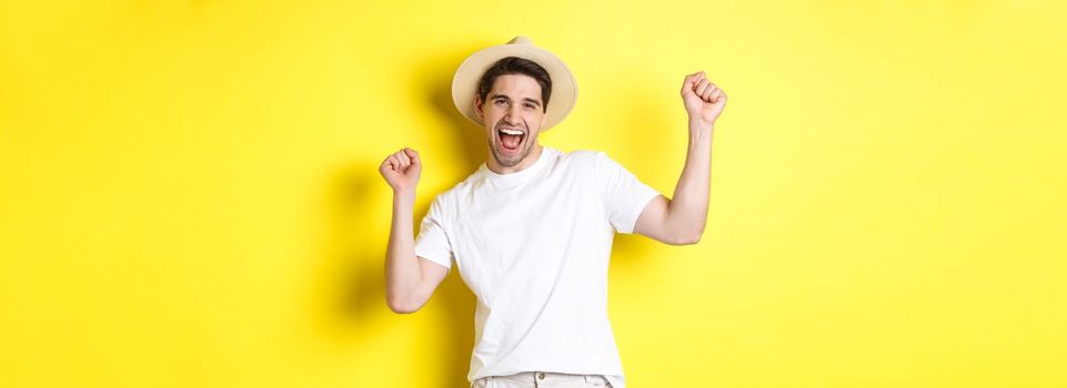 Concept of tourism and lifestyle. Happy man tourist celebrating, rejoicing over vacation, standing over yellow background.