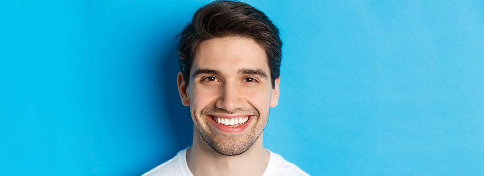 Head shot of handsome young man with beard, smiling happy over blue background. Copy space.