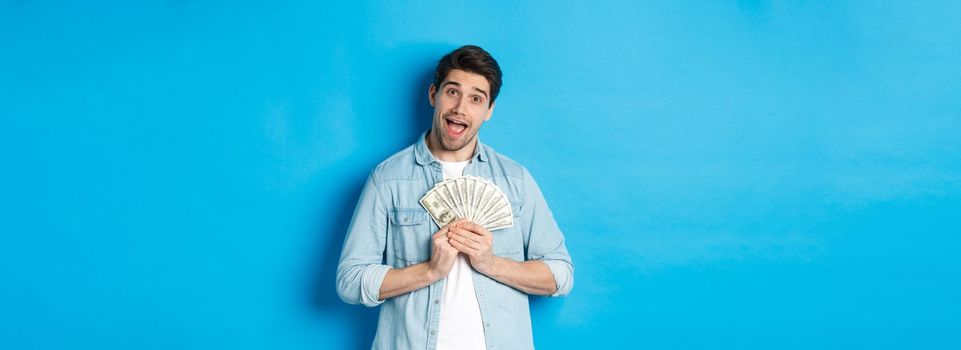 Smiling greedy guy hugging money and smiling, unwilling to share, standing over blue background.