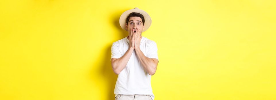 Concept of tourism and summer. Shocked guy jumping from fear, standing startled against yellow background.