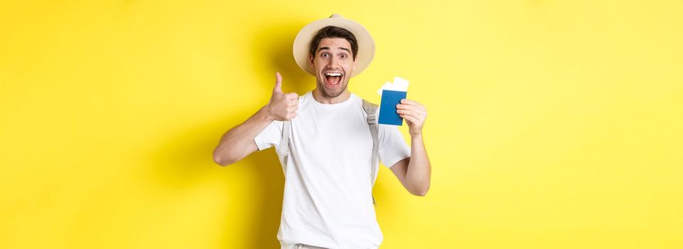 Tourism and vacation. Satisfied male tourist showing passport with tickets and thumb up, recommending travel company, standing over yellow background.