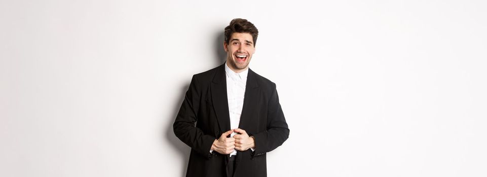 Concept of new year party, celebration and lifestyle. Portrait of handsome and confident man in suit, smiling pleased, feeling successful, standing over white background.