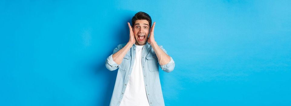 Scared man screaming and looking startled at something, standing against blue background.