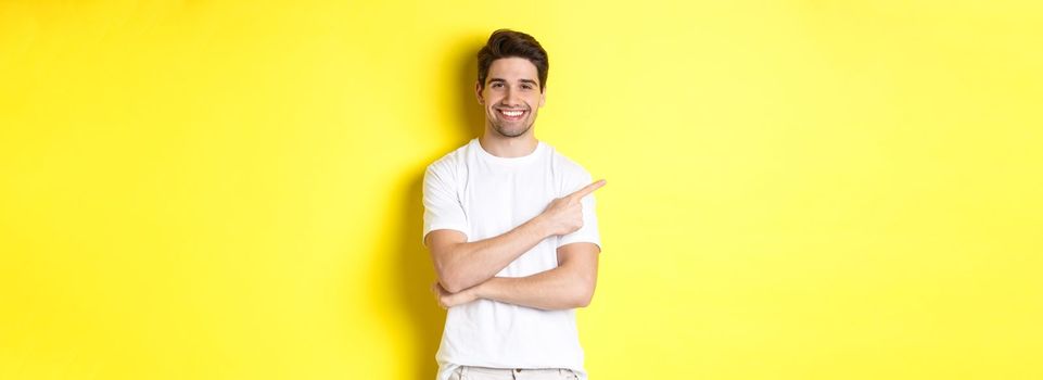 Handsome guy pointing left and smiling, showing advertisement on yellow copy space.