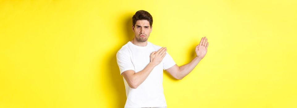 Man showing kung-fu skills, martial arts ninja movement, standing in white t-shirt ready to fight, standing over yellow background. Copy space