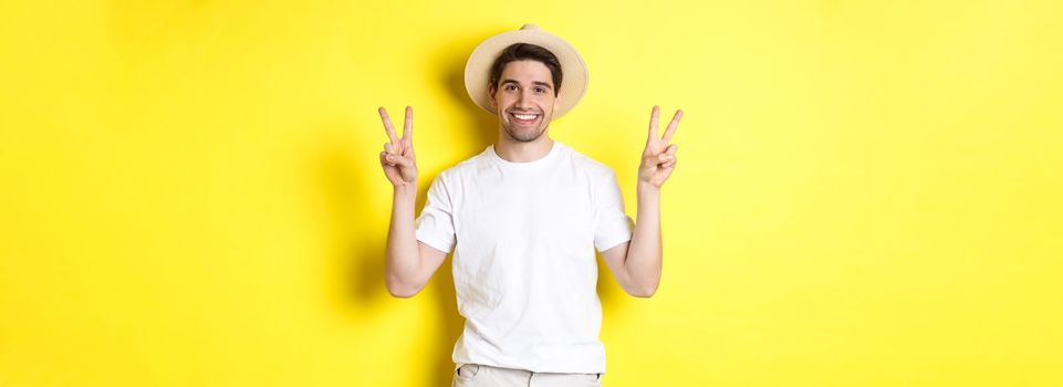 Concept of tourism and vacation. Happy male tourist posing for photo with peace signs, smiling excited, standing against yellow background.