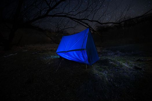 picnic tent at night. The family, mother and daughter, for the weekend went out into the countryside for a picnic, sit by the fire in the wild with a tent, fry potatoes, drink hot tea. High quality photo