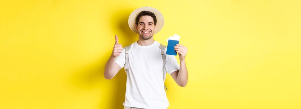 Tourism and vacation. Satisfied male tourist showing passport with tickets and thumb up, recommending travel company, standing over yellow background.