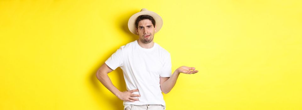 Concept of tourism and summer. Young skeptical tourist complaining, looking judgemental, standing over yellow background.