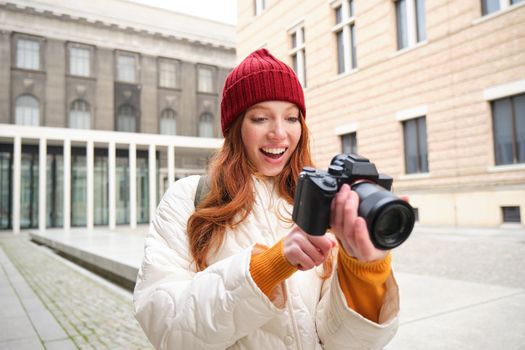 Beautiful readhead girl, photographer with professional camera takes pictures outdoors, walking around city and taking photos, sightseeing.