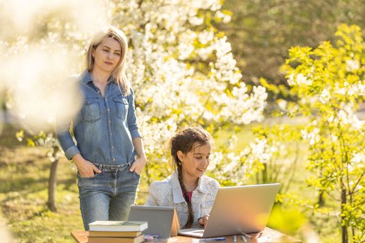 little girl with mom learning on laptop outdoor.