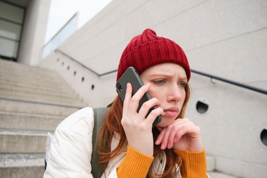 Portrait of worried girl calls somebody with concerned face, being on a phone, receives bad news, looking upset by conversation on smartphone.