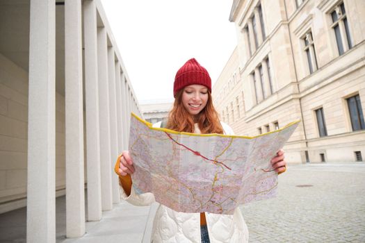 Redhead girl, tourist explores city, looks at paper map to find way for historical landmarks, woman on her trip around euope searches for sightseeing.