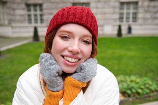 Cute girl student in red hat, warm gloves, sits in park, smiles and looks happy. Copy space