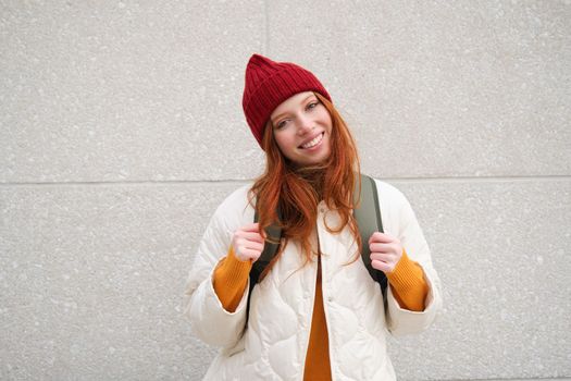 Happy young girl, redhead tourist in red hat with backpack, walks around town, explores city, backpacking around europe, travelling alone.