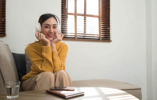 Smiling girl relaxing at home, she is playing music using a smartphone and wearing white headphones..