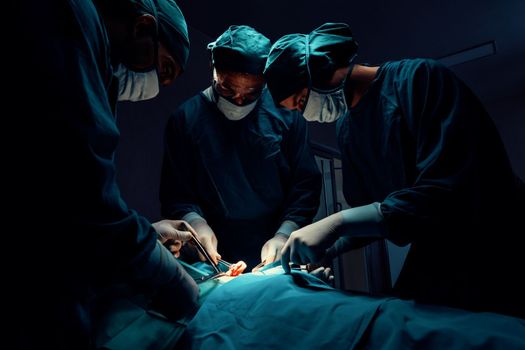 Surgical team performing surgery to patient in sterile operating room. In a surgery room lit by a lamp, a professional and confident surgical team provides medical care to an unconscious patient.