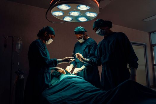 Surgical team performing surgery to patient in sterile operating room. In a surgery room lit by a lamp, a professional and confident surgical team provides medical care to an unconscious patient.