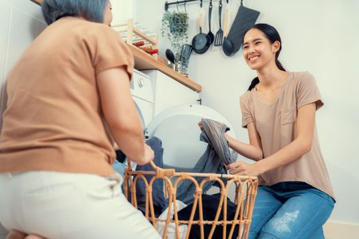 Daughter and mother working together to complete their household chores near the washing machine in a happy and contented manner. Mother and daughter doing the usual tasks in the house.