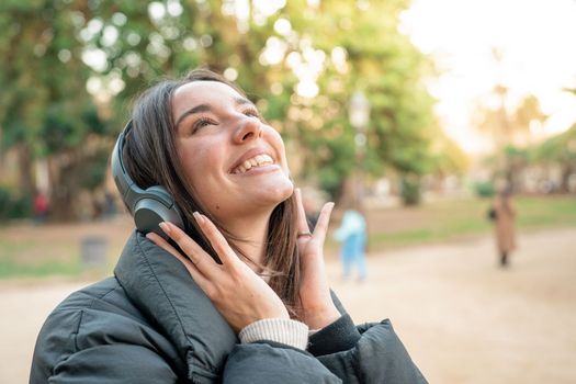 Attractive Woman Using Headphones listening to music, podcast or audio book outdoors in the park. Smiling happy people enjoying lifestyle.