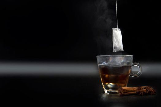 Glass of hot tea with tea bag hanging black background copy space, and cinnamon stick