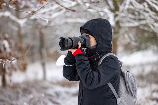 Woman with professional camera equipment taking a photo in winter forest, Germany