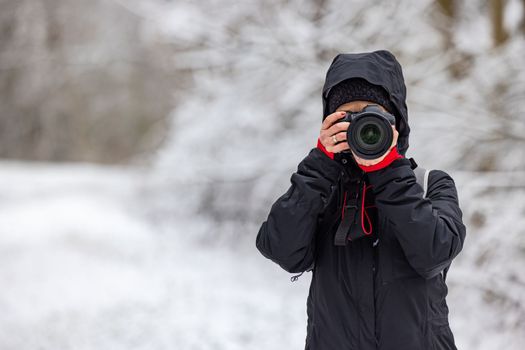 Woman photographer with professional camera shooting outdoors at winter time