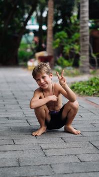 Boy blond freckles squatting sit smiling show gesture thumbs up shirtless bare chested shorts nature.