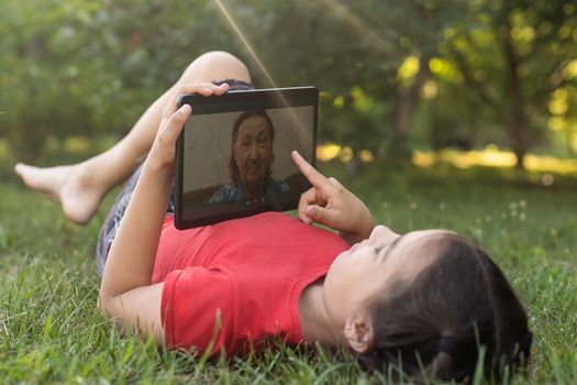 Child girl playing on a Digital tablet in the garden. Online or Remote education concept.