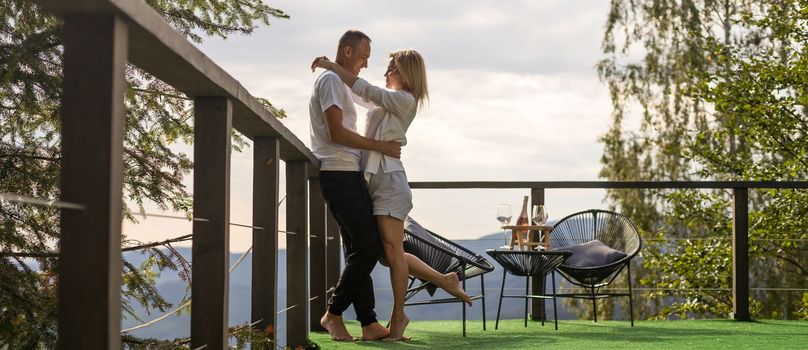 Horizontal sideview shot of a young couple in summer outfit enjoying the mountain view from terrace. Copy space