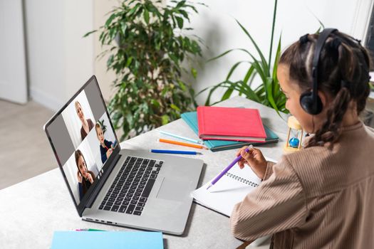 Child online. A little girl uses a laptop video chat to communicate learning while sitting at a table at home