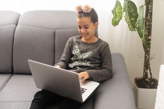 Caucasian Teenager girl, with a computer on a gray sofa in house