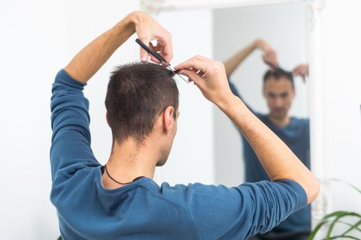 portrait of young man cutting himself hair indoor