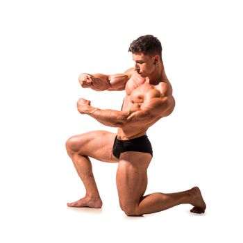 Young muscular male bodybuilder posing in briefs, in studio shot against neutral background