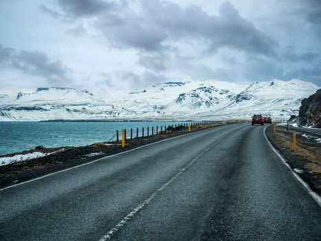 Car riding on asphalt countryside road towards magnificent snowy mountains during trip through Iceland, next to ocean shore