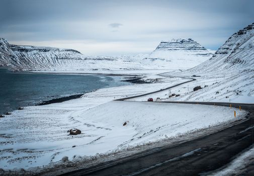 Car riding on asphalt countryside road towards magnificent snowy mountains during trip through Iceland, next to ocean shore