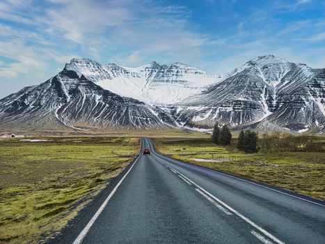 Car riding on asphalt countryside road towards magnificent snowy mountains during trip through Iceland